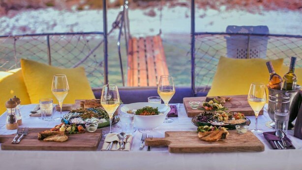 Une table dressée pour un repas, avec différents plats et des verres de vin, donnant sur un paysage magnifique.