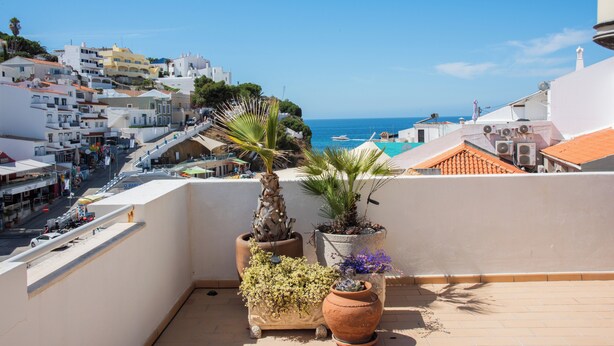 Un balcón con macetas, con vistas a un pueblo costero con edificios y un cielo azul claro.