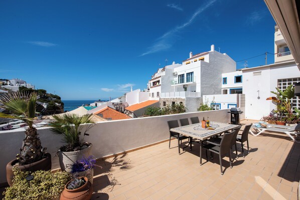 Terraza en la azotea con mesa y sillas, plantas en macetas y vistas al mar y edificios.