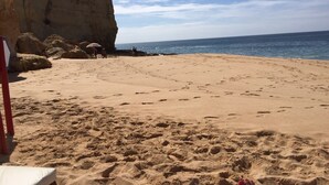 Una playa arenosa con huellas, un acantilado y algunas personas al fondo.