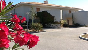 Un edificio de dos plantas con techo de tejas, pared de piedra y un pequeño jardín con flores rojas.