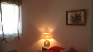 Un dormitorio con una cama, una mesita de noche, una lámpara, una ventana con cortinas y un cuadro en la pared.