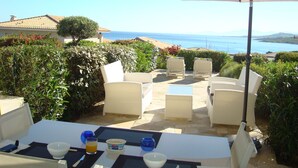 Un patio exterior con una mesa preparada para dos personas, con vistas panorámicas al mar y las colinas.