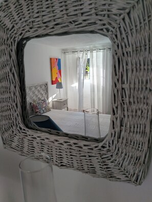Ein Schlafzimmer mit einem Bett, einem Nachttisch, einer Lampe, einem farbenfrohen Gemälde und einem Fenster mit durchsichtigen Vorhängen.