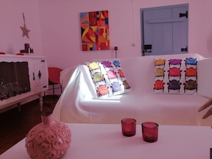 Una stanza con un divano bianco, cuscini colorati, un vaso decorativo e un quadro appeso al muro.