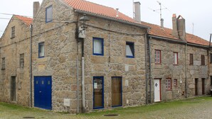 Un edificio in pietra con tetto in tegole rosse, diverse finestre e una porta blu.