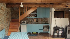 Una cucina compatta con una scala in legno, una zona pranzo con tovaglia a quadri e una televisione fissata al muro.