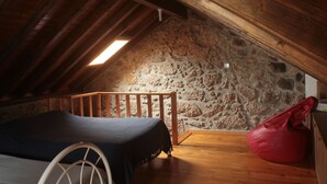 Una camera da letto mansardata accogliente, con soffitto in legno, parete in pietra, un letto e una borsa rossa.
