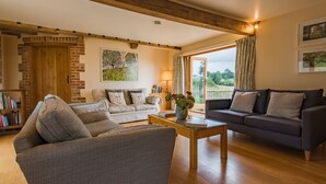 A cozy living room with a wooden ceiling, a brick wall, a wooden door, a sofa, a coffee table, and a bookshelf. - Converted barn / Oast House with amazing views and EV chargers (Rye)
