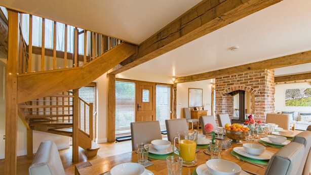 A dining area with a wooden staircase, brick fireplace, and a table set for four with plates, glasses, and a fruit bowl. - Converted barn / Oast House with amazing views and EV chargers (Rye)