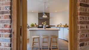 A kitchen with a central island, wooden stools, a hanging light fixture, and a tiled backsplash. - Converted barn / Oast House with amazing views and EV chargers (Rye)