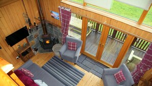 Ein gemütliches Zimmer mit Kamin, zwei grauen Sessel, einer Couch und einem Fernseher.