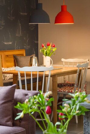 A dining area with a round table, white chairs, a red pendant light, and a wall with sailboat illustrations.