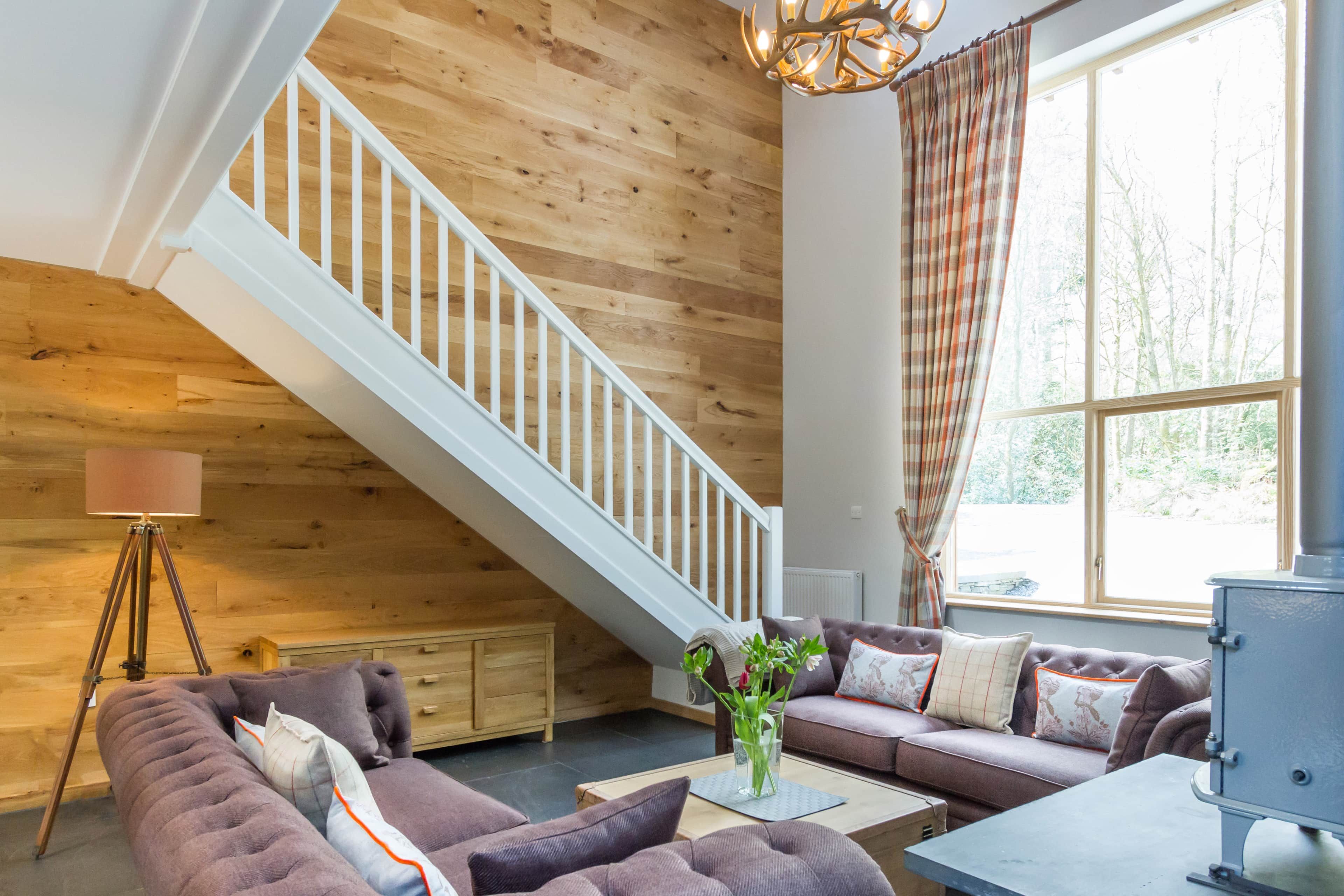 A spacious living room with a high ceiling, a staircase, a fireplace, and a large window with curtains.