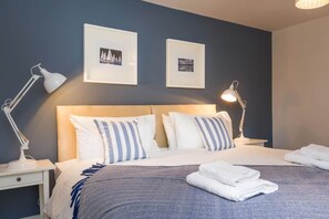 A neatly made bed with striped pillows, a bedside lamp, and a folded towel on a nightstand. - The Cedars (Ambleside)