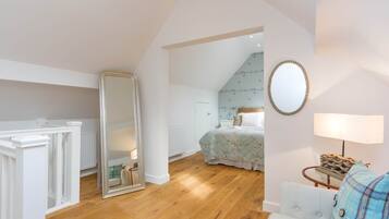 A bedroom with a large mirror, a bed with a floral duvet, a wooden floor, and a white dresser.