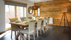 A dining area with a wooden table and chairs, a hanging light fixture, and a view of the outdoors.