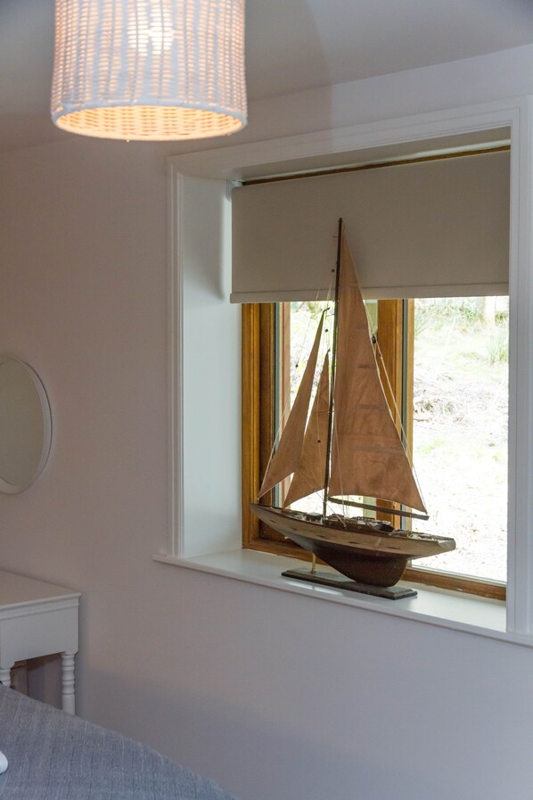 A model sailboat on a windowsill with a view of a natural landscape.