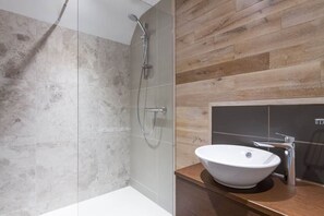 A modern bathroom with a shower, a sink, and a wooden wall. - The Cedars (Ambleside)