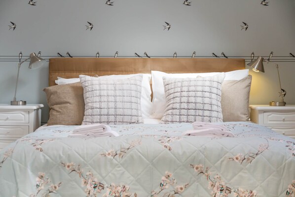 Un lit avec une couette à motifs floraux, deux oreillers blancs et une tête de lit en bois.