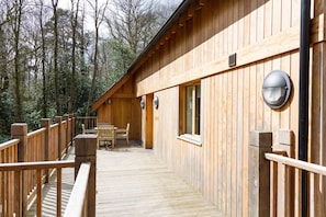 A wooden deck leading to a cabin with a table and chairs, surrounded by trees. - The Cedars (Ambleside)