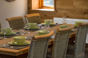 A dining table set with green plates, bowls, and wine glasses, surrounded by woven chairs.
