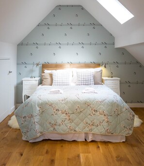 A bedroom with a sloped ceiling, a bed with floral bedding, two bedside tables, and a skylight.