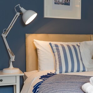Un lit bien fait, agrémenté d’oreillers à rayures, une lampe de chevet blanche et un tableau encadré au mur.
