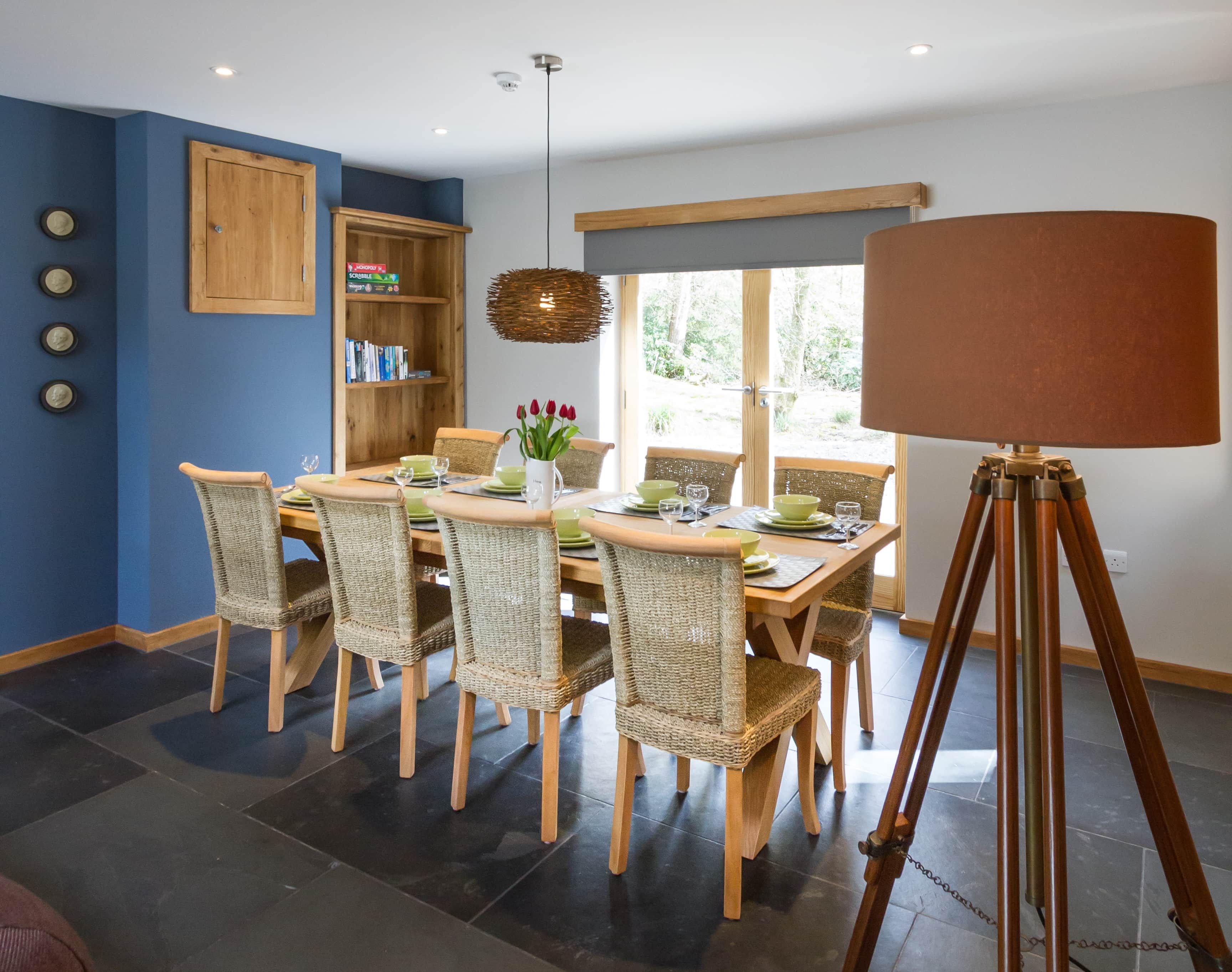 A dining area with a wooden table, wicker chairs, and a tripod-mounted lamp.