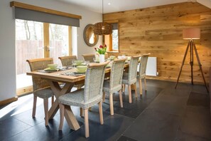 A dining area with a wooden table and chairs, a floor lamp, and a large mirror on the wall. - The Cedars (Ambleside)