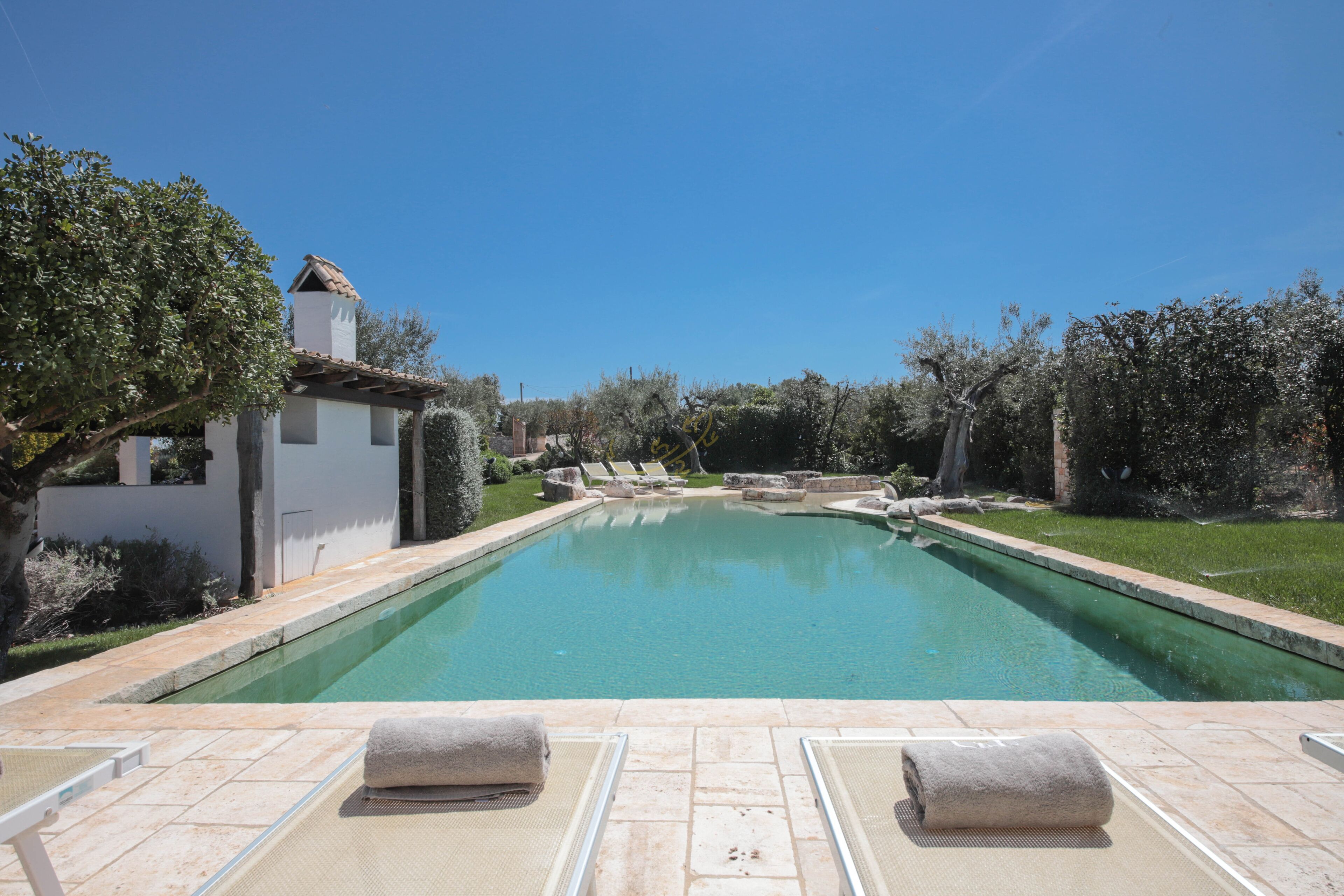 Une piscine avec des chaises longues et un petit bâtiment doté d’un toit en tuiles.