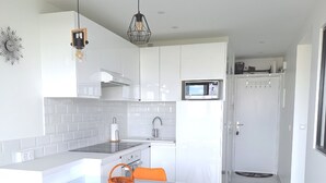 A modern kitchen with white cabinetry, a glass dining table, and orange chairs. - Arcachon beautiful 12m2 terrace with Harbour View and beach Classified 3 * (Arcachon)