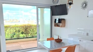 A modern kitchen with a glass dining table, orange chairs, and a view of a garden through a sliding door. - Arcachon beautiful 12m2 terrace with Harbour View and beach Classified 3 * (Arcachon)