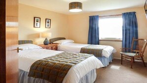 A hotel room with two beds, a wooden chair, a nightstand, a lamp, and a window with curtains.
