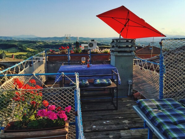 Una terraza en la azotea con una mesa lista para dos personas, una sombrilla roja y vistas al campo.