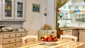 A dining area with a table set for four, a bowl of fruit, and a view into the kitchen. - Casa Marola, house with character (Gabicce Mare)