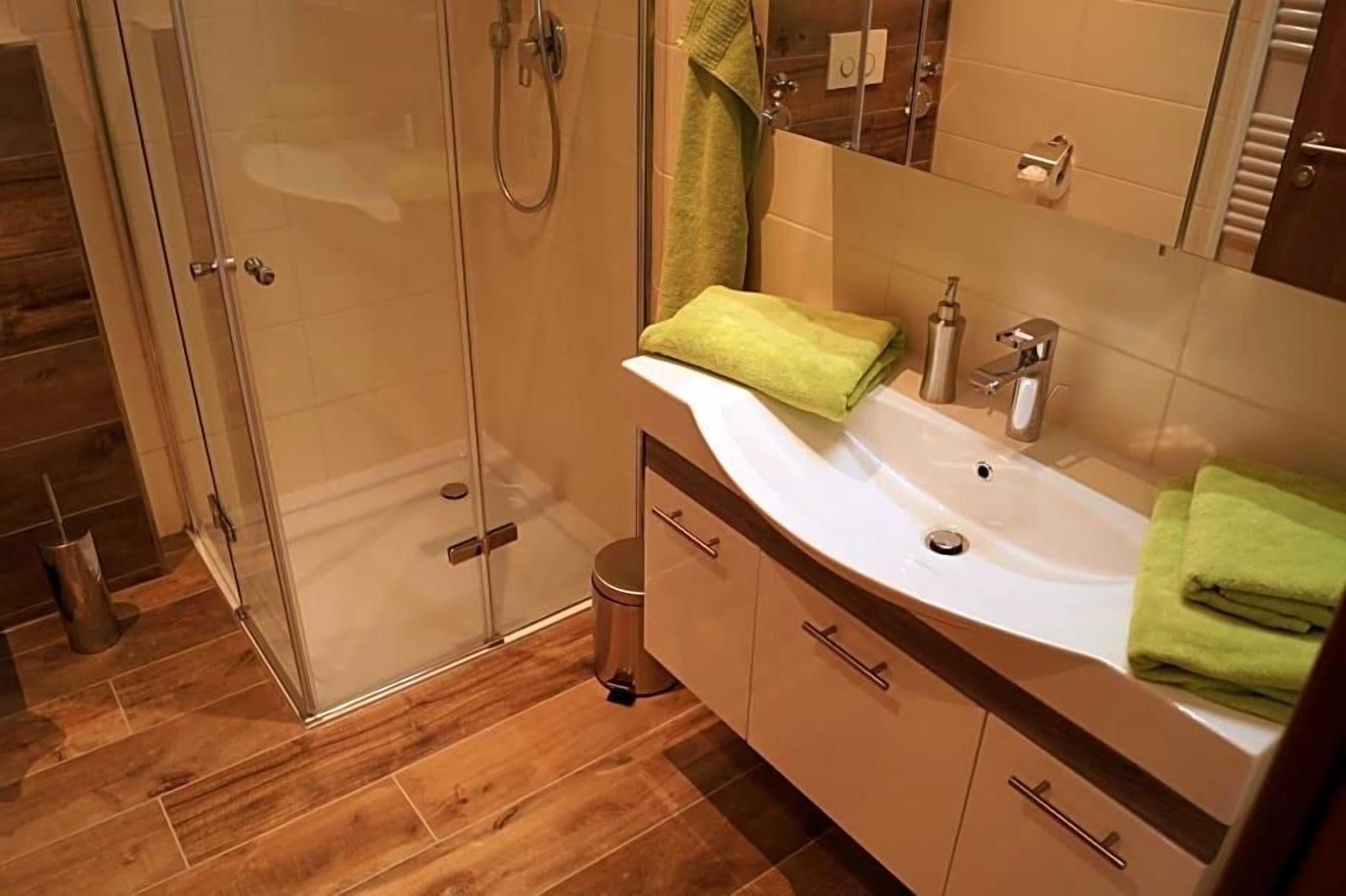 Een moderne badkamer met een douchecabine van glas, een wit wastafelmeubel en een houten vloer.