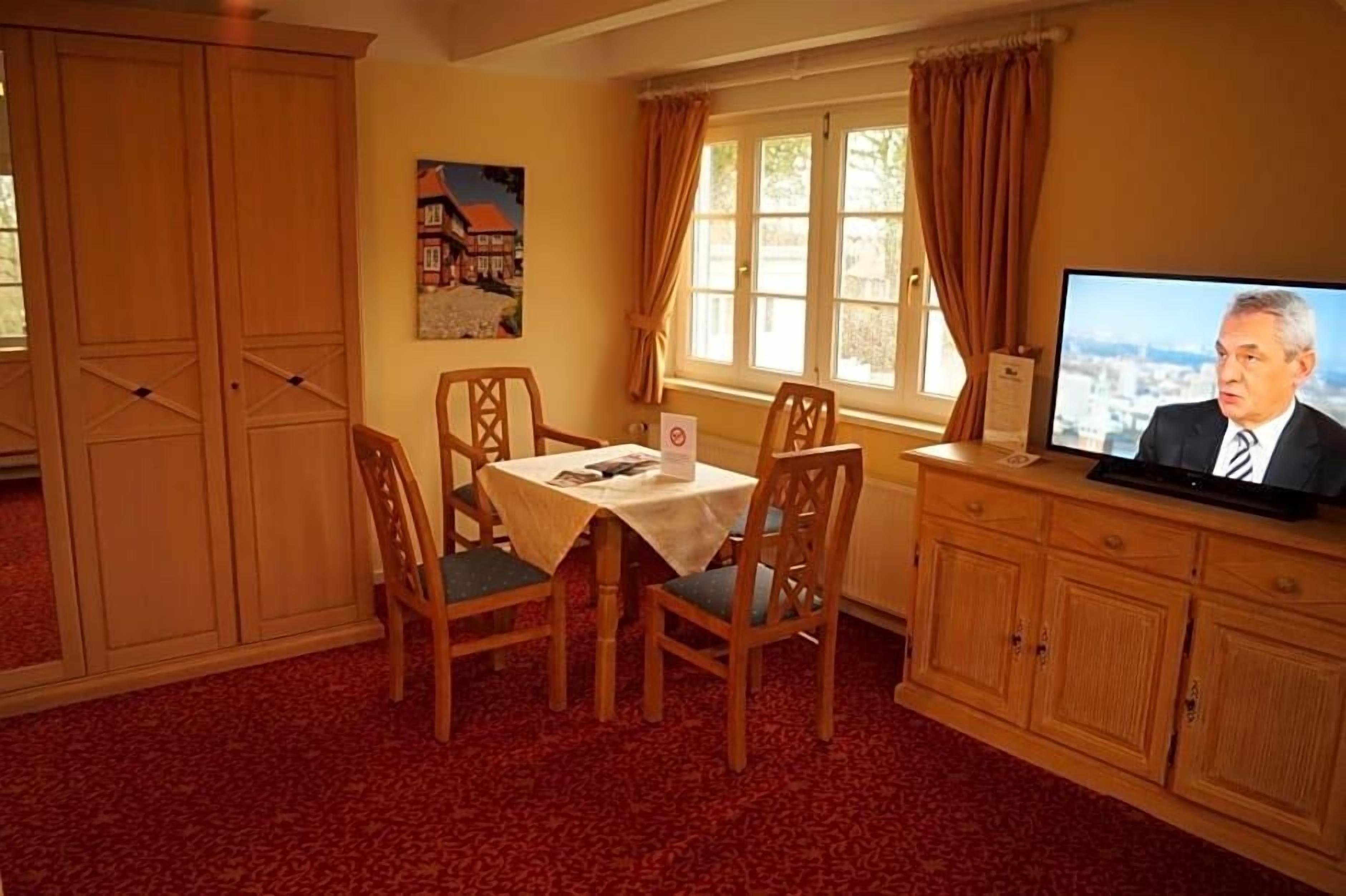 Een kamer met een eettafel, stoelen, een televisie en een raam met gordijnen.