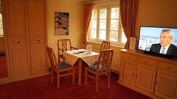 Een kamer met een eettafel, stoelen, een televisie en een raam met gordijnen.
