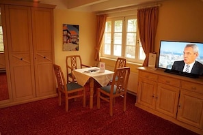 A room with a dining table, chairs, a television, and a window with curtains.