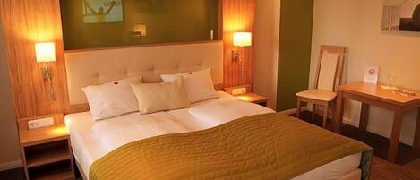 Ein Hotelzimmer mit einem großen Bett, zwei Nachttischen, einem Schreibtisch und einem Sessel.