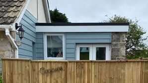 A wooden fence with the word "Coop" written on it, a house with a stone foundation, and a gravel driveway. - Coppice, Entire 1 bedroom annex, pet friendly. EV Charger.  (Barton on Sea)