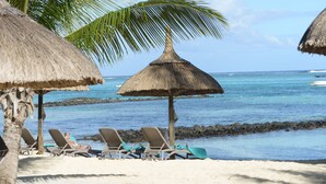 A beach with thatched umbrellas, lounge chairs, and a clear view of the ocean. - Flic En Flac: Spacious Villa in a Tranquil Environment - Close to Amenities (Flic en Flac)