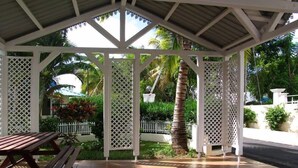 A covered outdoor area with a wooden bench, a white lattice structure, and a palm tree. - Flic En Flac: Spacious Villa in a Tranquil Environment - Close to Amenities (Flic en Flac)