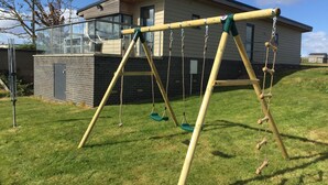 Un portique en bois se trouve dans une cour verdoyante, avec une maison en arrière-plan.