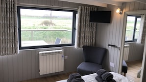 Une chambre avec une grande fenêtre, un fauteuil, un lit avec des serviettes pliées, une télévision et un radiateur.