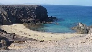 A rocky beach with clear blue water and a large cliff. - Spacious Villa with Private, Sunny Garden, Sea View and Exclusive Pool  (Playa Blanca)