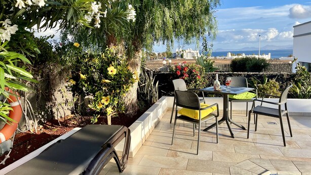 A terrace with a table and chairs, a pool, and a view of the sea and buildings. - Spacious Villa with Private, Sunny Garden, Sea View and Exclusive Pool  (Playa Blanca)