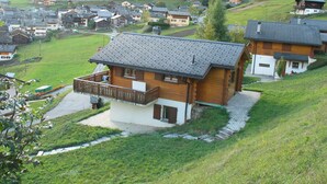 Ein Holzhaus mit Balkon, umgeben von einer grünen Landschaft und anderen Häusern.