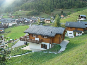 Ein Holzhaus mit Balkon, umgeben von einer grünen Landschaft und anderen Häusern.